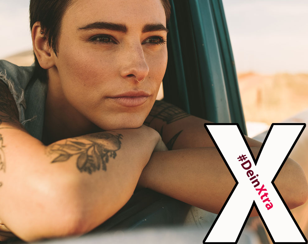 #DeinXtra | Bild zeigt eine mittelalte Frau im Auto mit Tattoos, die in die Ferne schaut. | © AdobeStock: Jacob Lund
